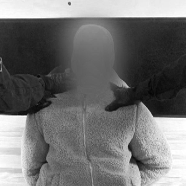 Den misstänkte mannen sitter bojad medan två poliser håller tag i honom. Mannens ansikte är pixlat och bilden svartvit.