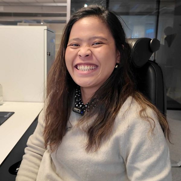 En ung kvinna sitter vid ett skrivbord på ett kontor och ser glad ut, efter att ha blivit anställd på ett nytt företag efter att hon tappade jobbet på Norhvolt.