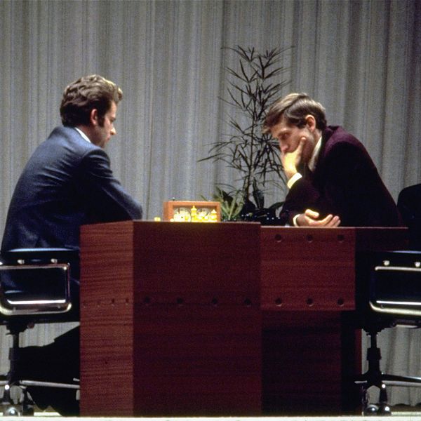 Två män spelar schack vid ett bord, djupt koncentrerade.