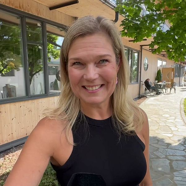 Blond kvinna tittar in i kameran och ler.
