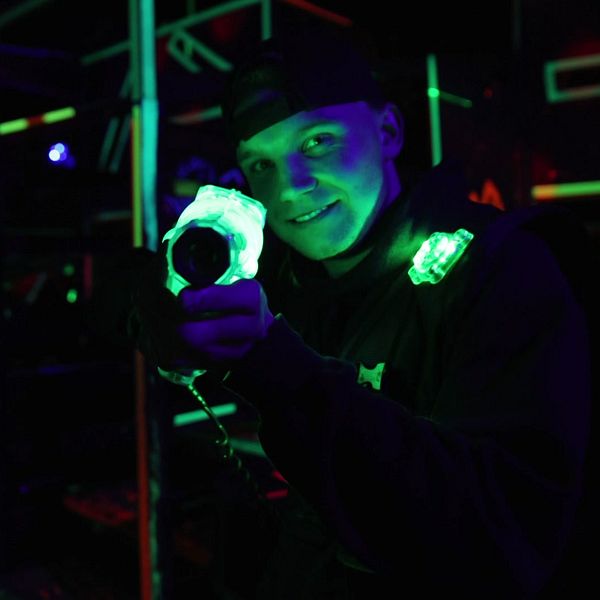 Person deltar i en lasertag-match, lysande utrustning i mörk miljö.