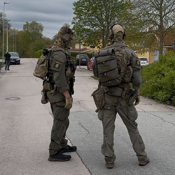 Två tungt beväpnade poliser står på en avspärrad gata i bostadsområde.