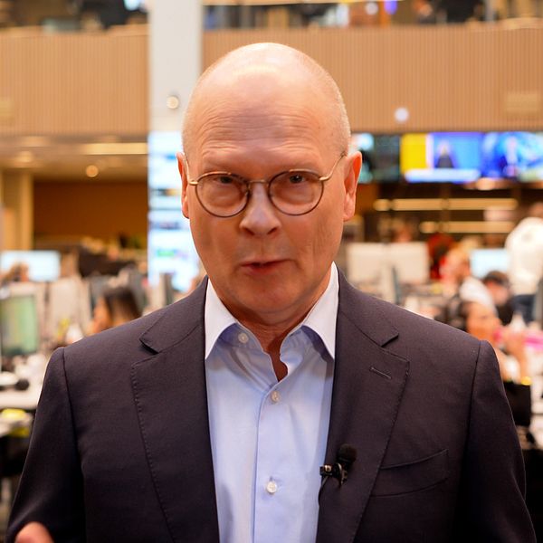 Person i kostym i stor kontorsmiljö fylld med datorskärmar och personal.