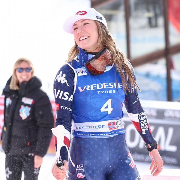 En glad Mikaela Shiffrin i tävlingsdräkt och champagneflaska i handen.