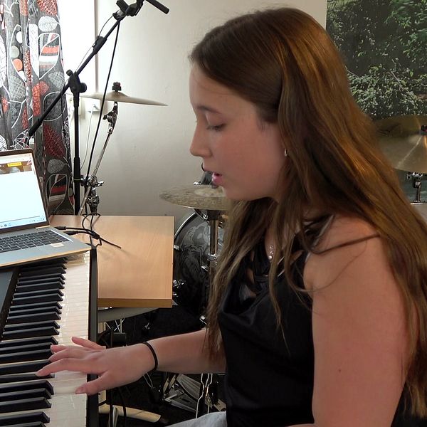Lilly Sundström i svart linne på kulturskolan i Arjeplog. Hon sitter och spelar piano framför en dataskärm.