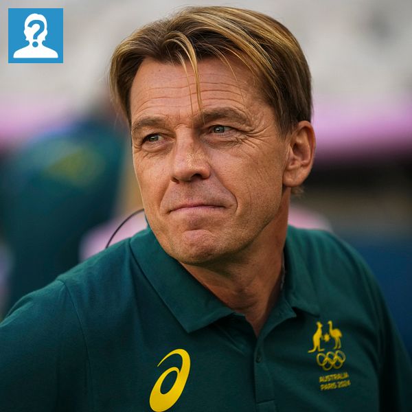 En person iklädd en grön tröja med Australiens olympiska logotyp står utomhus. I bakgrunden syns en suddig grupp av människor, varav en i en tröja med guldfärgade inslag.