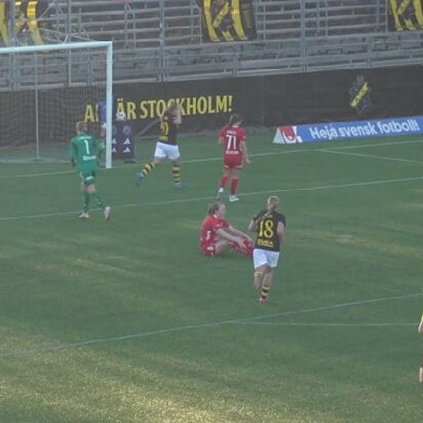 Fotbollsspelare på plan, en sitter ner nära målet. Domare i gul tröja i förgrunden.