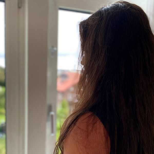 En mörkhårig kvinna tittar ut genom fönstret