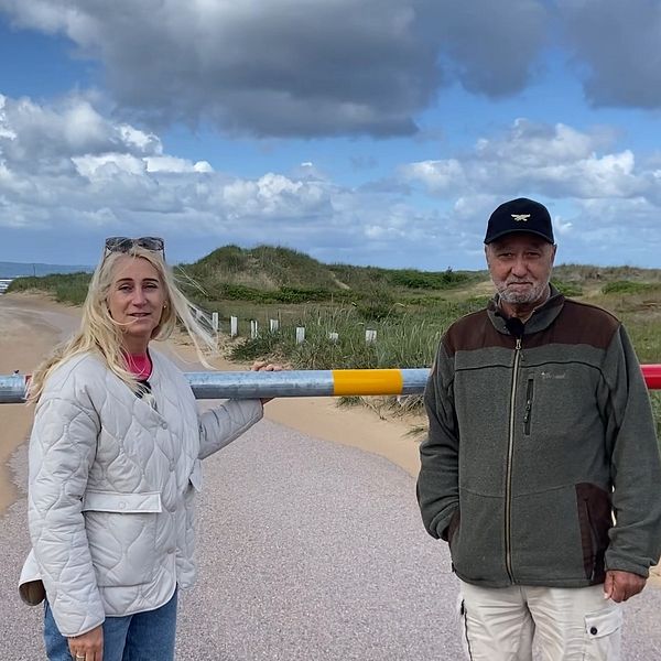 Chatarina Friiberg och Bengt Sjöberg står framför bommen de har tvingats sätta upp mot sin vilja vid den före detta bilstranden i Mellbystrand.