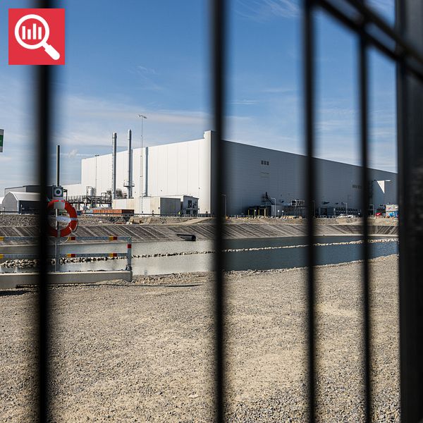 Industrianläggning bakom stängsel med vattenkanal i förgrunden.