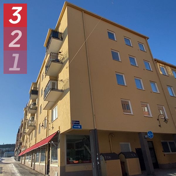 Ett femvåningshus med ljusgul fasad och balkonger ligger på en gata under en klarblå himmel. Gatan är delvis snötäckt och sträcker sig in mot fjärran.