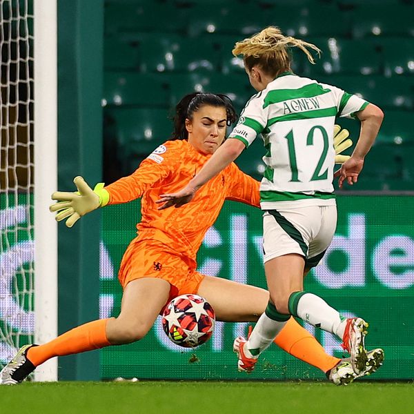 En fotbollsspelare i grönvitrandigt skjuter mot mål förbi målvakt i orange matchställ.