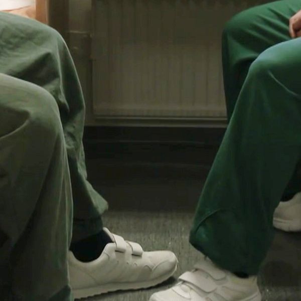 Två personer, anonymiserade, sitter i en häktescell med gröna häkteskläder.
