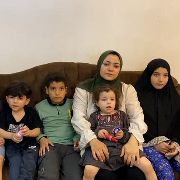 Mamma med fem barn sitter i en brun soffa
