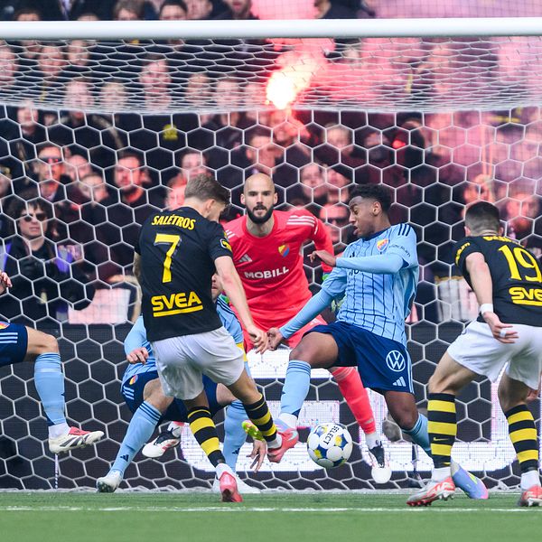 AIK och Djurgården-spelare slåss om bollen framför mål, publik med bengaler i bakgrunden.