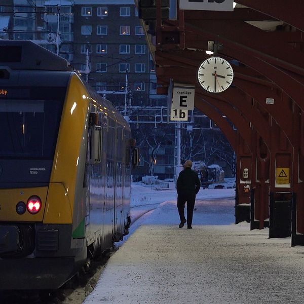 Ett tåg står vid en snötäckt perrong. Konduktören går på perrongen bredvid tåget