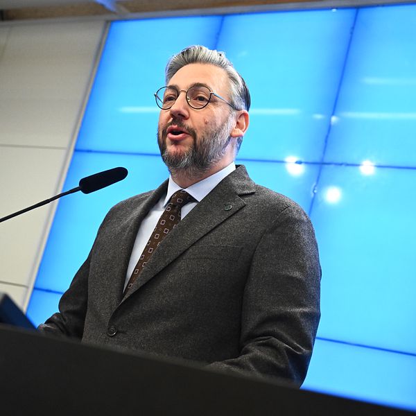 Man i kostym står vid podie med mikrofon framför blå bakgrund.  Centerpartiets partiledare Muharrem Demirok meddelar under en pressträff på måndagen att han kommer att avgå.