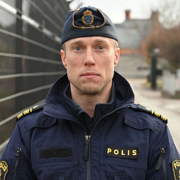 Polis i uniform vid stängsel på en mulen dag.