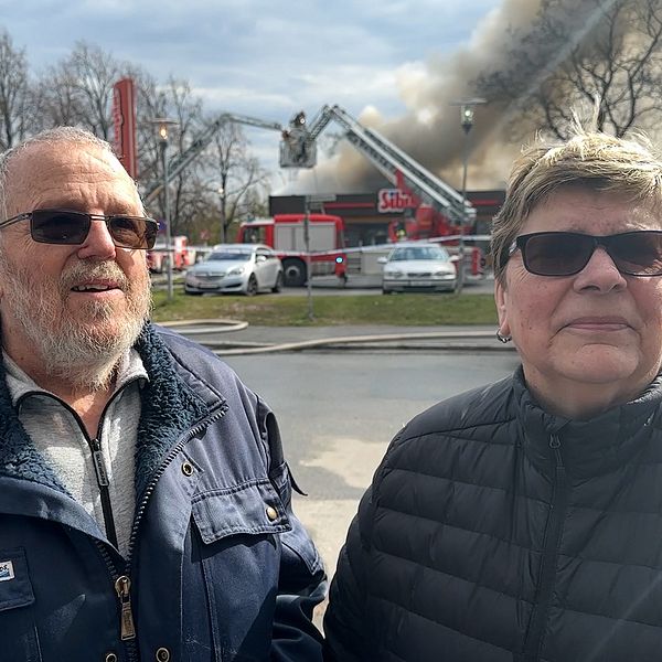 Två personer som står framför den brinnande Sibyllarestuarangen i Örebro.