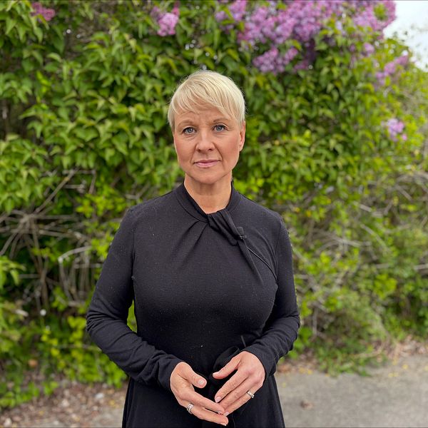 Äldre- och socialförsäkringsminister Anna Tenje (M) står framför blommande buskar utomhus.