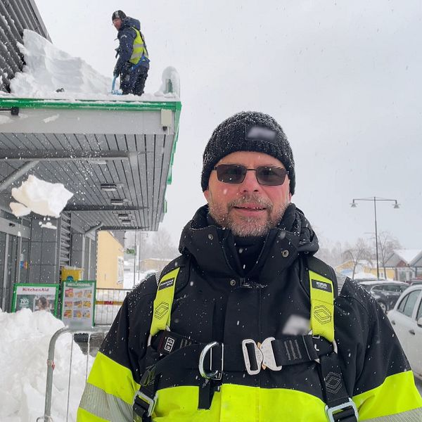 En klättrande skottare står framför en man som skottar taket på en butik.