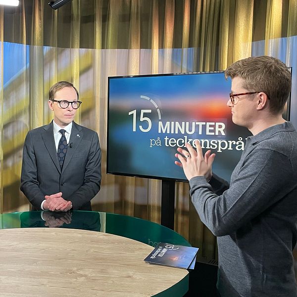 Magnus Bergevin, Mats Persson och en teckenspråkstolk står vid ett runt bord i en studio.