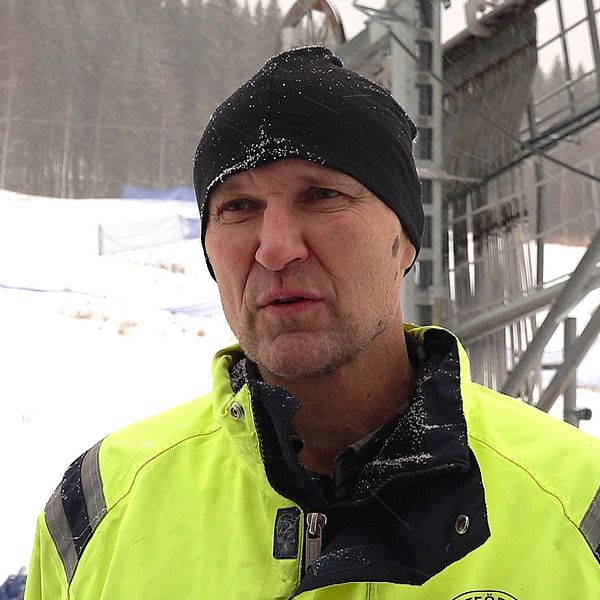 Mattias Wikner står i en gul arbetsjacka i en snöig miljö, framför liftanläggningen i Persåsen med snötäckta träd i bakgrunden.