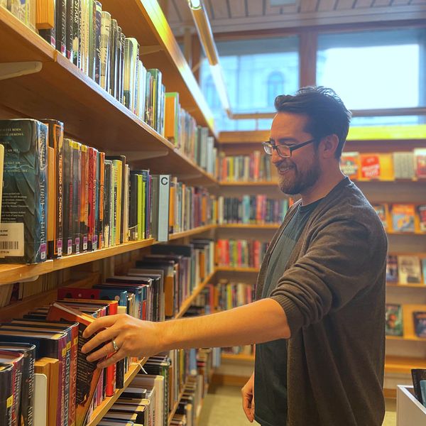 En man vid en bokhylla på ett bibliotek pillar på en bok.