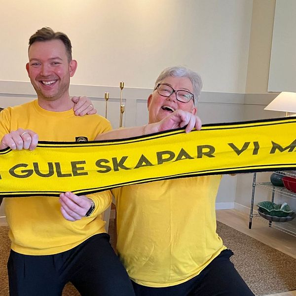 Tre personer sitter bredvid varandra och håller upp en gul halsduk med texten ”FÖR DI GULE SKAPAR VI MAGI”. De två personerna på sidorna har på sig gula tröjor.