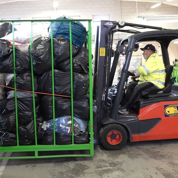En person kör truck och flyttar bur fylld med svarta sopsäckar på återvinningscentral.