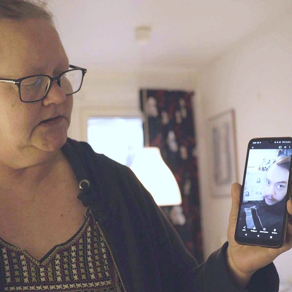 Tims mamma Anita står i en lägenhet och håller uppe en mobil med en bild på Tim.