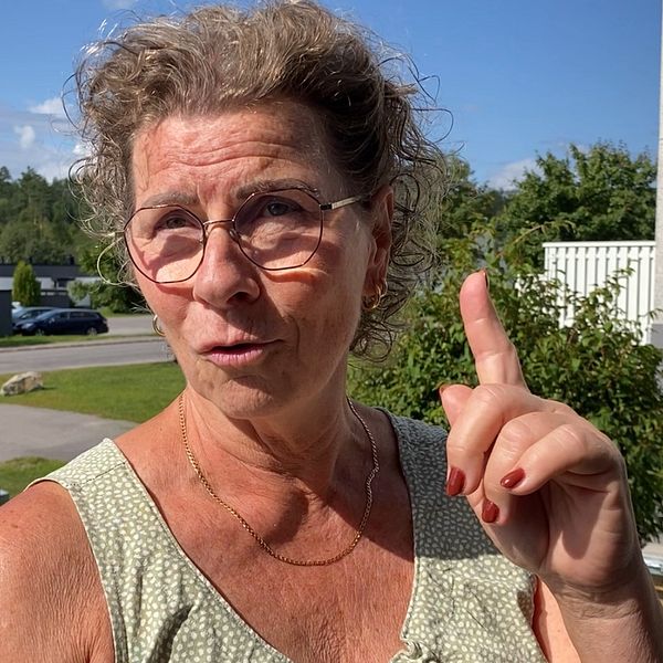 Åsa Melander står utanför sin lägenhet och pekar med ett finger upp i luften