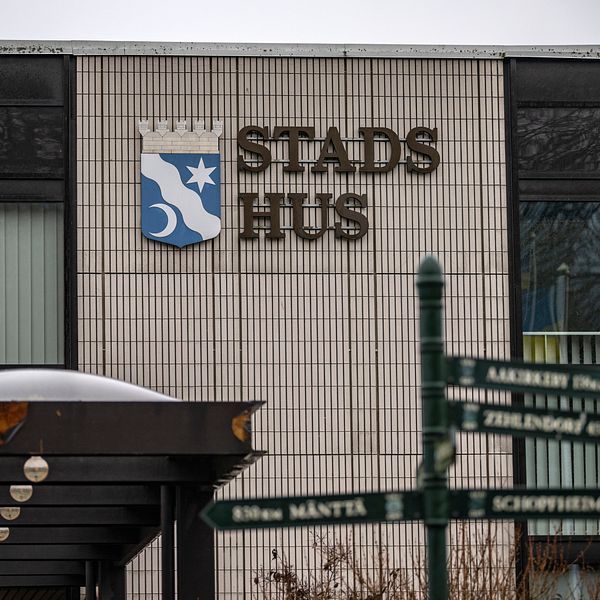 Stads Hus-skylt på en byggnad med en vägskylt i förgrunden som visar riktningar.