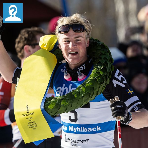 Skidåkare firar med krans och banderoll efter lopp, publik i bakgrunden.