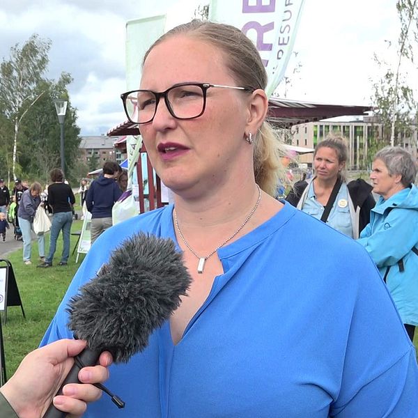 En porträttbild på kommunalrådet Carina Sammeli (S) i blå tröja och svarta glasögon. Många människor i bakgrunden.