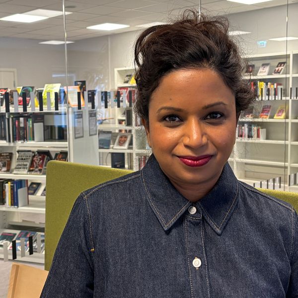 En person står i en modern biblioteksinteriör omgiven av hyllor fyllda med böcker.