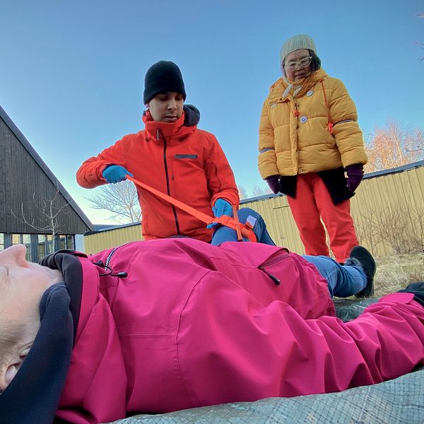Personer övar första hjälpen utomhus, en person ligger ned medan två står och instruerar.