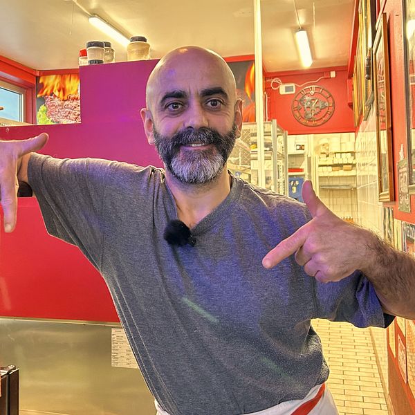 Özay ”Lillen” Özcelik står i sin pizzarestaurang i Sundsvall, ser glad ut och pekar nedåt med pekfingrarna.