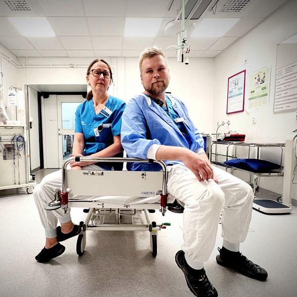 Två sjukvårdsanställda sitter på en brits i ett sjukhusrum.