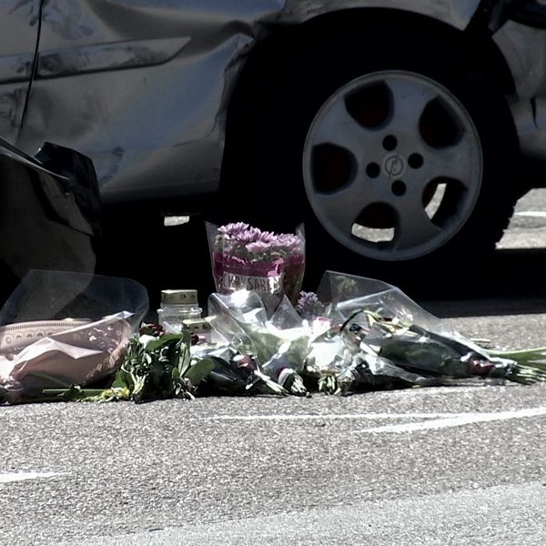Blombuketter ligger på marken framför en bil