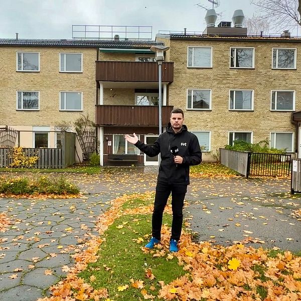 Man står på en innergård framför ett flerfamiljshus i höstmiljö.