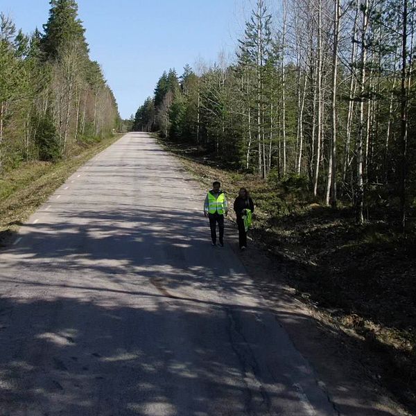 Två personer med reflexväst går på en väg med en blodfläck på.