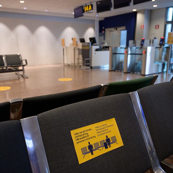 Tomt väntrum på en flygplats med avståndsskyltar på sittplatserna. En informationsskylt på en av bänkarna visar rekommendationer för avstånd mellan passagerare för att förhindra spridning av smitta.
