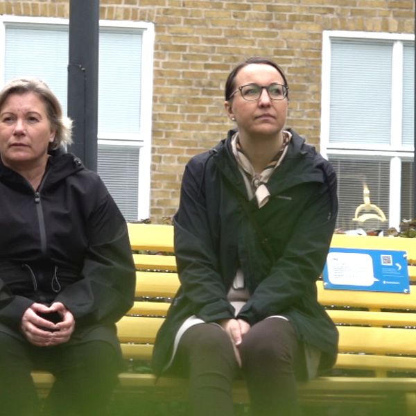 Två kvinnor sitter på en gul bänk.