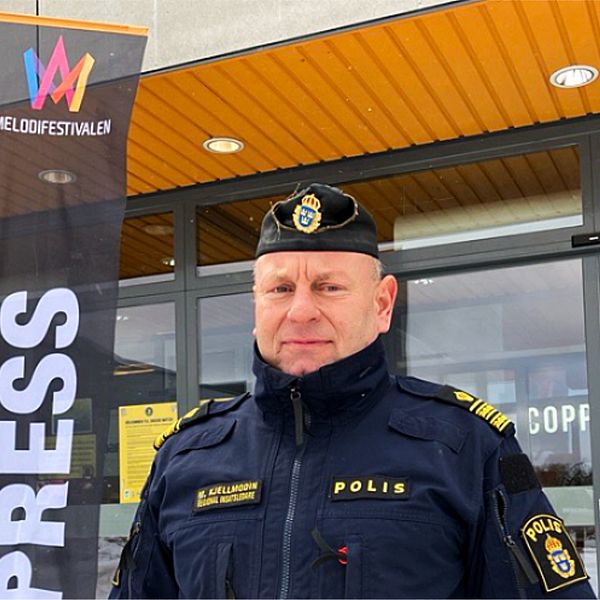 En polisuniformerad person står utanför en byggnad med ett ”PRESS”-flaggstång i bakgrunden.