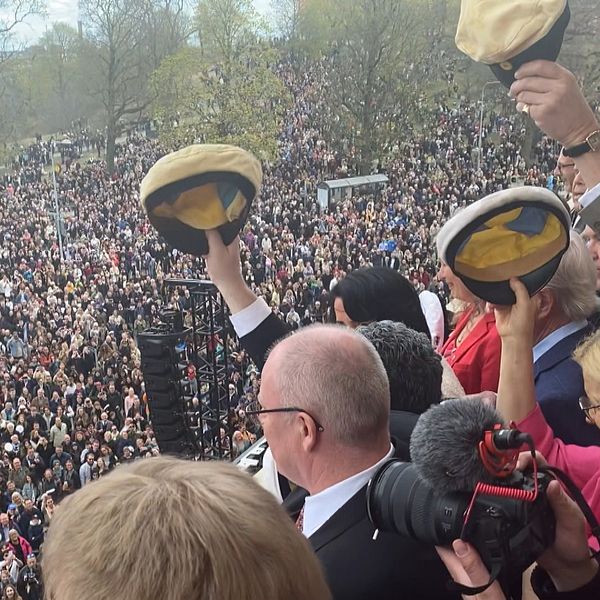 Personer med studentmössor i händerna och ett folkhav.