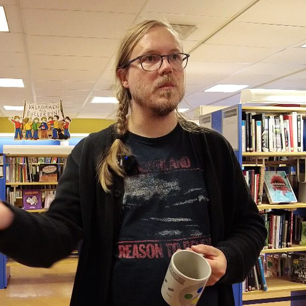 En bibliotekarie står med en kopp i den ena handen och håller ut den andra handen