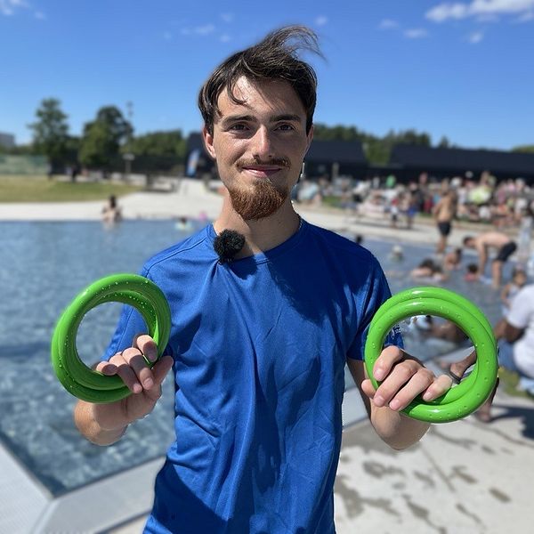 En man står med badringar framför en utomhuspool