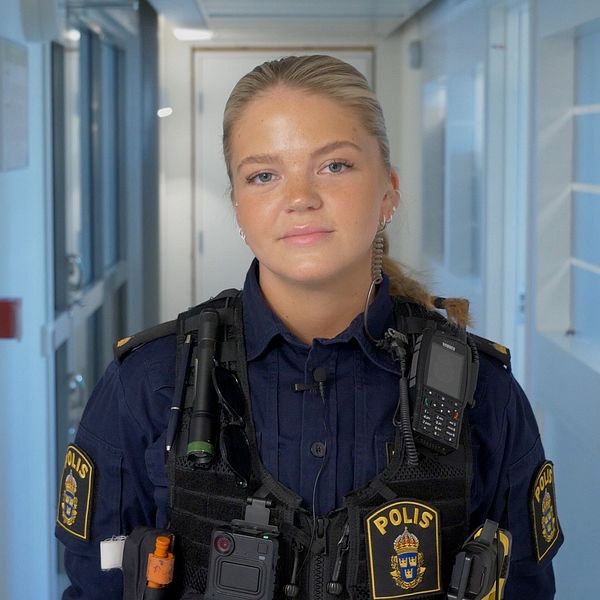 Polis i uniform står i en korridor med ljusa väggar och fönster.
