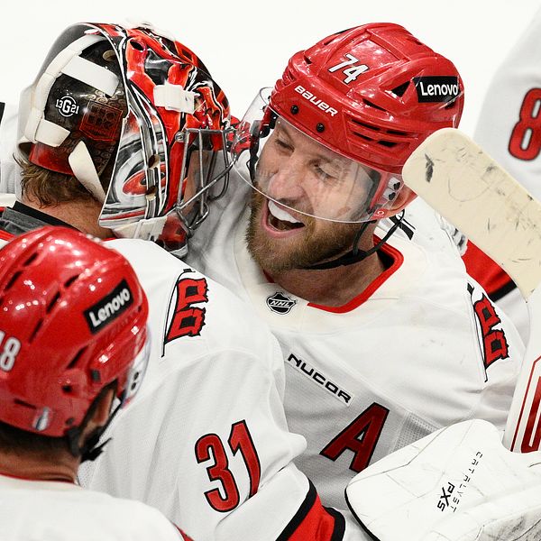Ishockeyspelare i rödvita matchställ kramar om varandra och firar på isen.